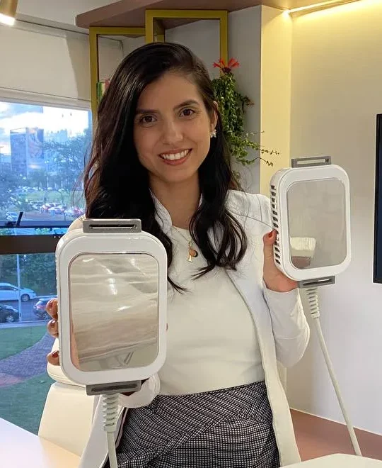 Patrícia Abrahão, de jaleco branco, segura os dois aplicadores de frio na sala do Instituto, com a janela para Brasília ao fundo.